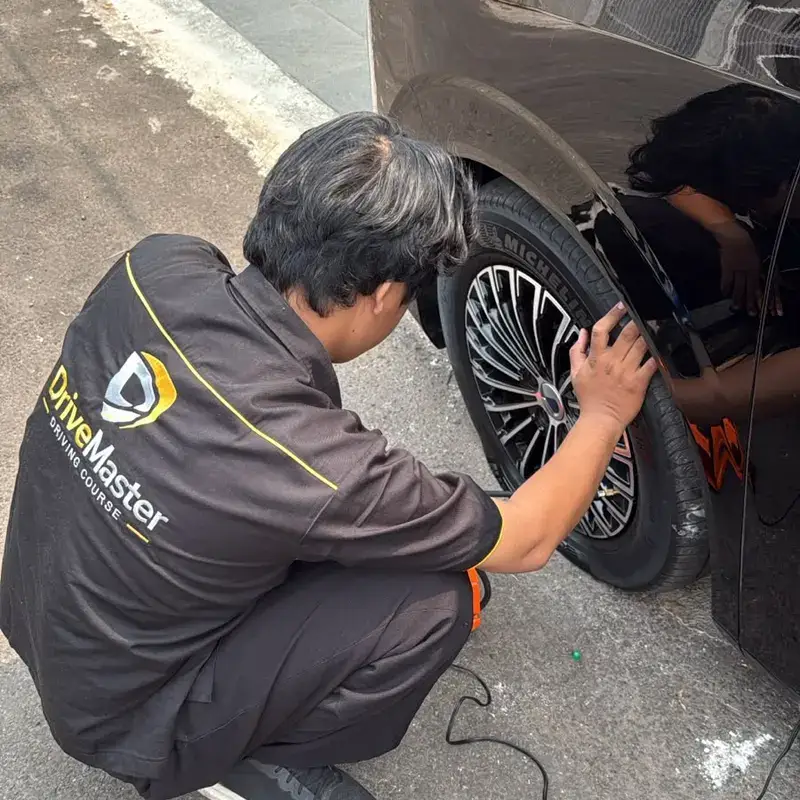 Teknisi berseragam DriveMaster menangani roda mobil di lokasi