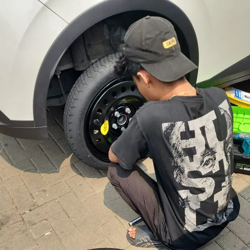 Teknisi memasang ban serep hitam pada mobil putih
