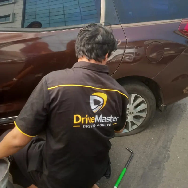 Teknisi berseragam DriveMaster bekerja di samping roda mobil